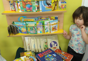 Nasza biblioteczka z książkami. Zuzia wybiera książkę.