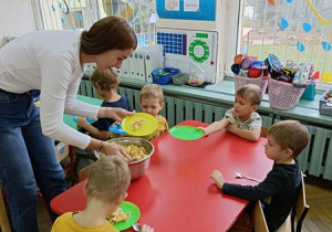 Ciocia Karolina częstuje sałatką przy czerwonym stoliku.