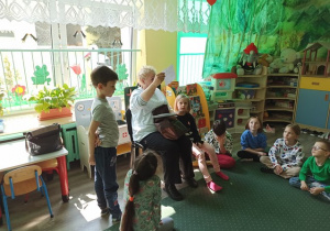 Pani Krysia pokazuje dzieciom kolorowanki, które im przyniosła