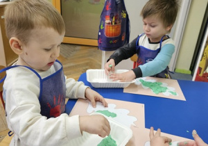 Chłopcy wyklejają liście zieloną masą solną.