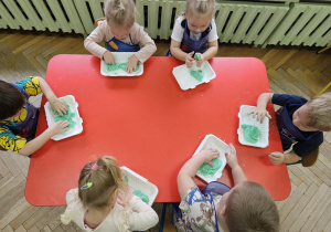 Zabawy z zieloną masą solną przy czerwonym stole.