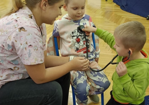 Mateusz bada Jasia stetoskopem.