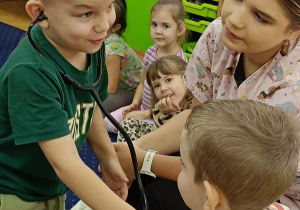 Mikołaj bada Jasia stetoskopem.