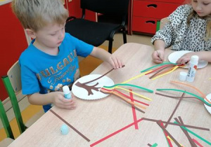 Kajtek i Maja przyklejają kolorowe paski.