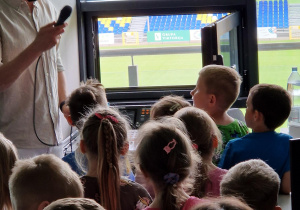 Przedszkolaki z zaciekawieniem podziwiają stadion przez spikerskie okno.